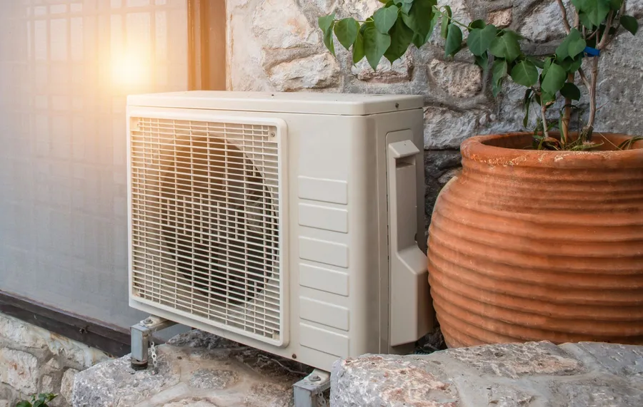 AC outdoor unit installed beside a stone wall and terracotta pot on a Mediterranean property