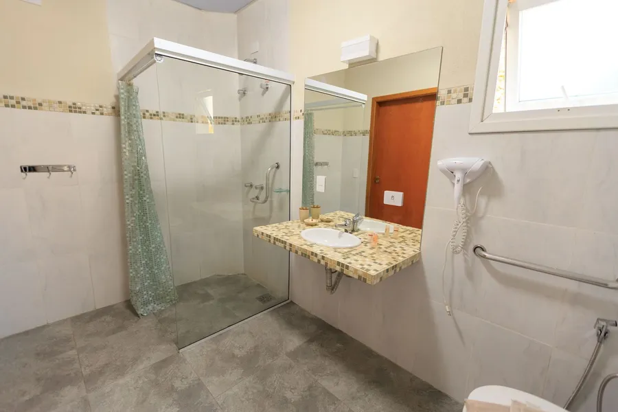 Bathroom with a glass-screened shower on a flush tiled floor and stainless steel grab rails fixed to the wall
