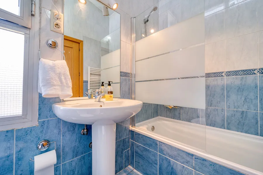 Tiled apartment bathroom with a pedestal basin, a bath with a glass screen and a heated towel rail