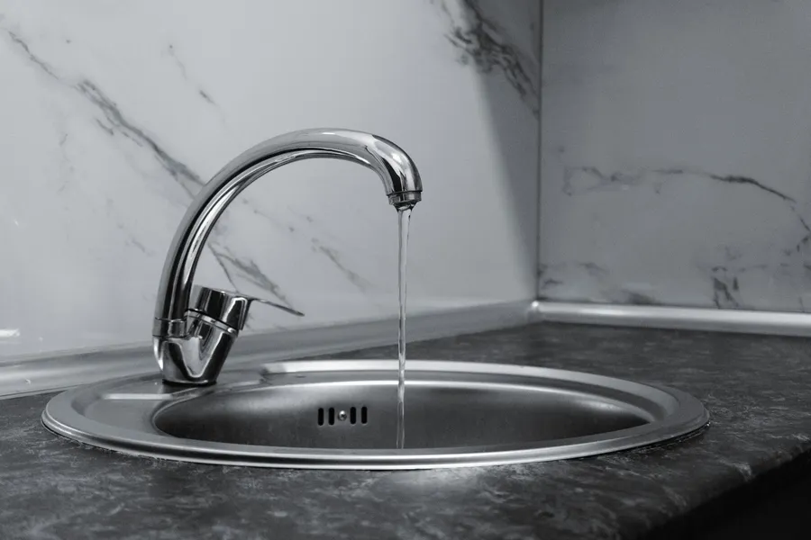 Chrome single-lever mixer tap running cold water into a round stainless steel kitchen sink