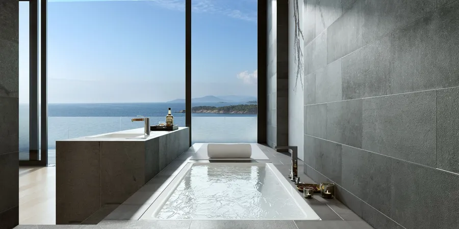 Grey stone bathroom with a built-in bath beside a full-height window looking out over the sea