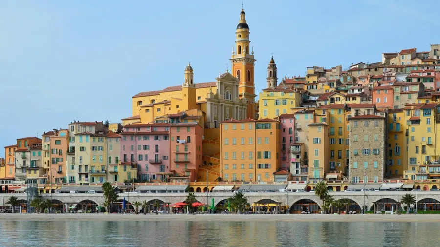 Old-town apartment buildings in pastel render stacked above the seafront in Menton