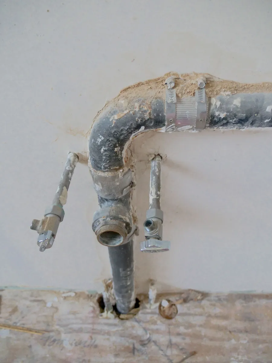 Old corroded metal supply pipes and a cast drain pipe in a plastered wall