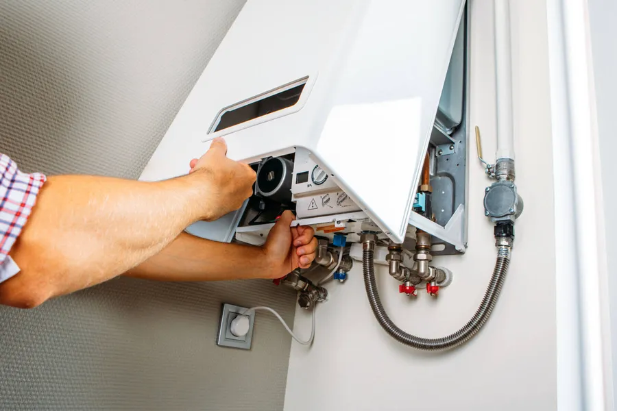 Plumber servicing a wall-mounted water heater system in a residential property