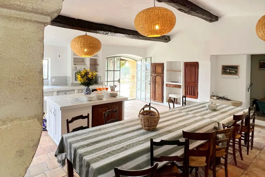 Renovated Provençal farmhouse kitchen with a tiled island, terracotta floor, beams and an arched door onto the garden