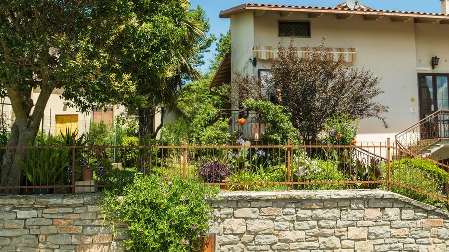Rust-coloured metal railing on a low stone wall in front of a rendered house and garden