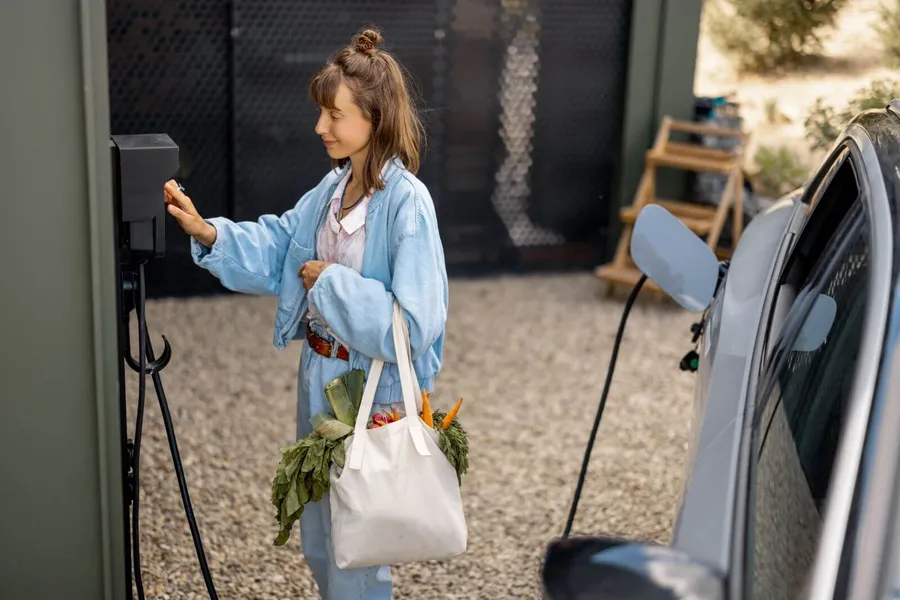 Woman plugging a Type 2 charging cable into her electric vehicle at a home charging point